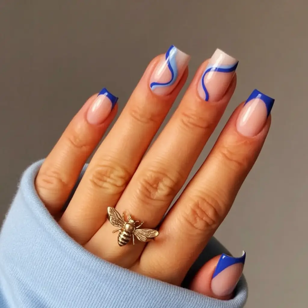 stylish blue spring nails for 2026 Bold Blue French Tips with Graphic Swirl Accents