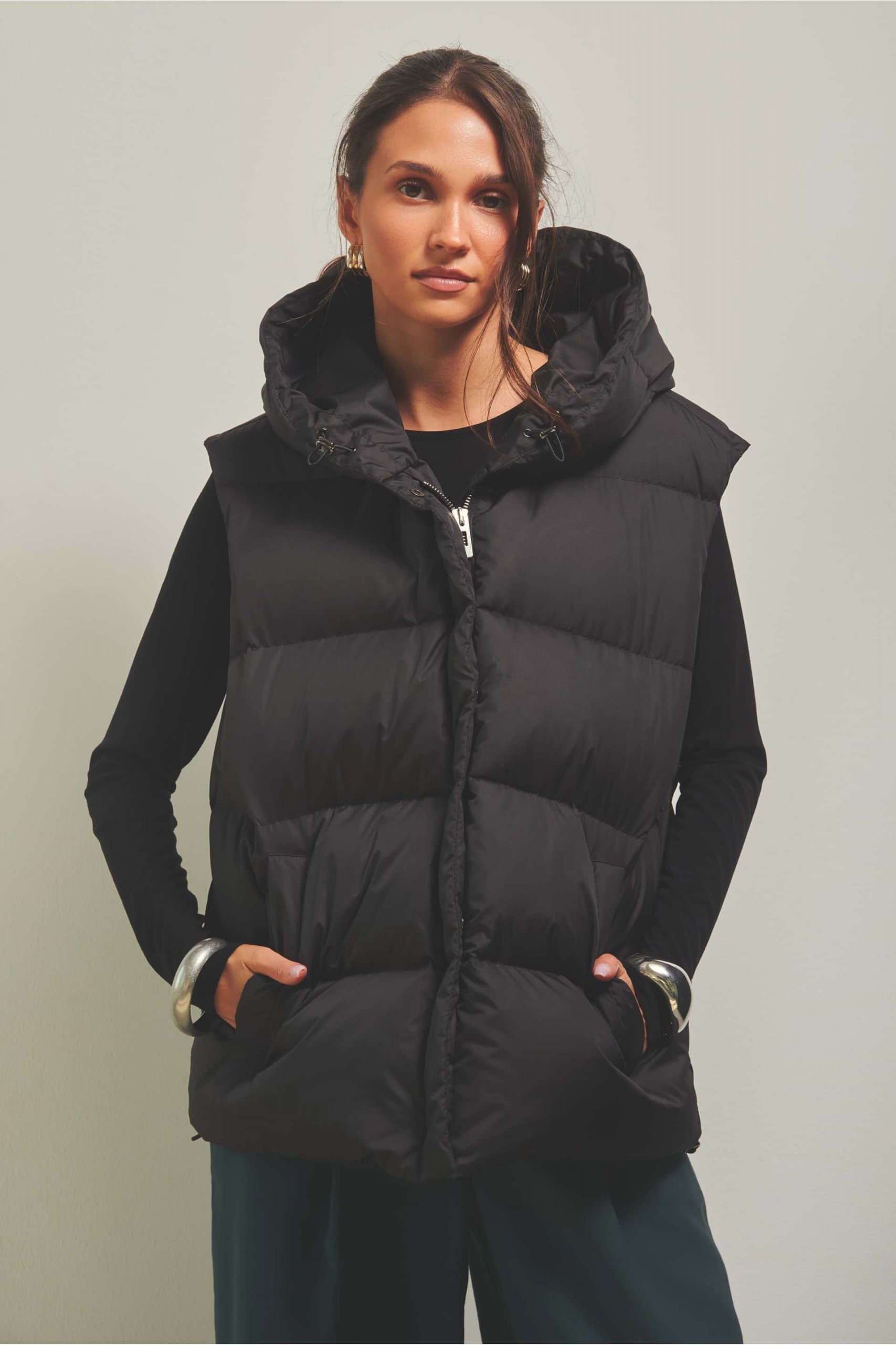 Black Hooded Puffer Vest Over Long-Sleeved Top with Teal Trousers — Puffer Vest Outfits