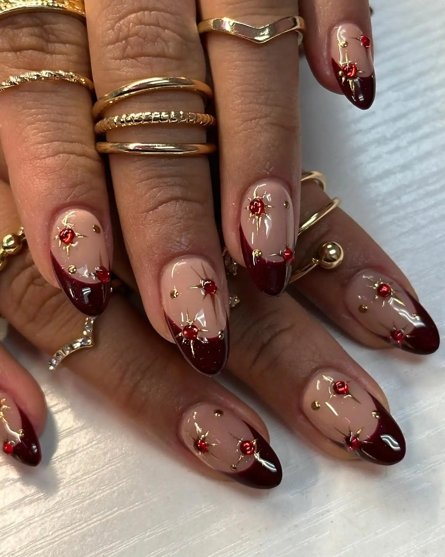 Nude French Tips with Red Gems and Gold Studs Nude French Tips with Red Gems and Gold Studs — Burgundy Christmas Nails 2026